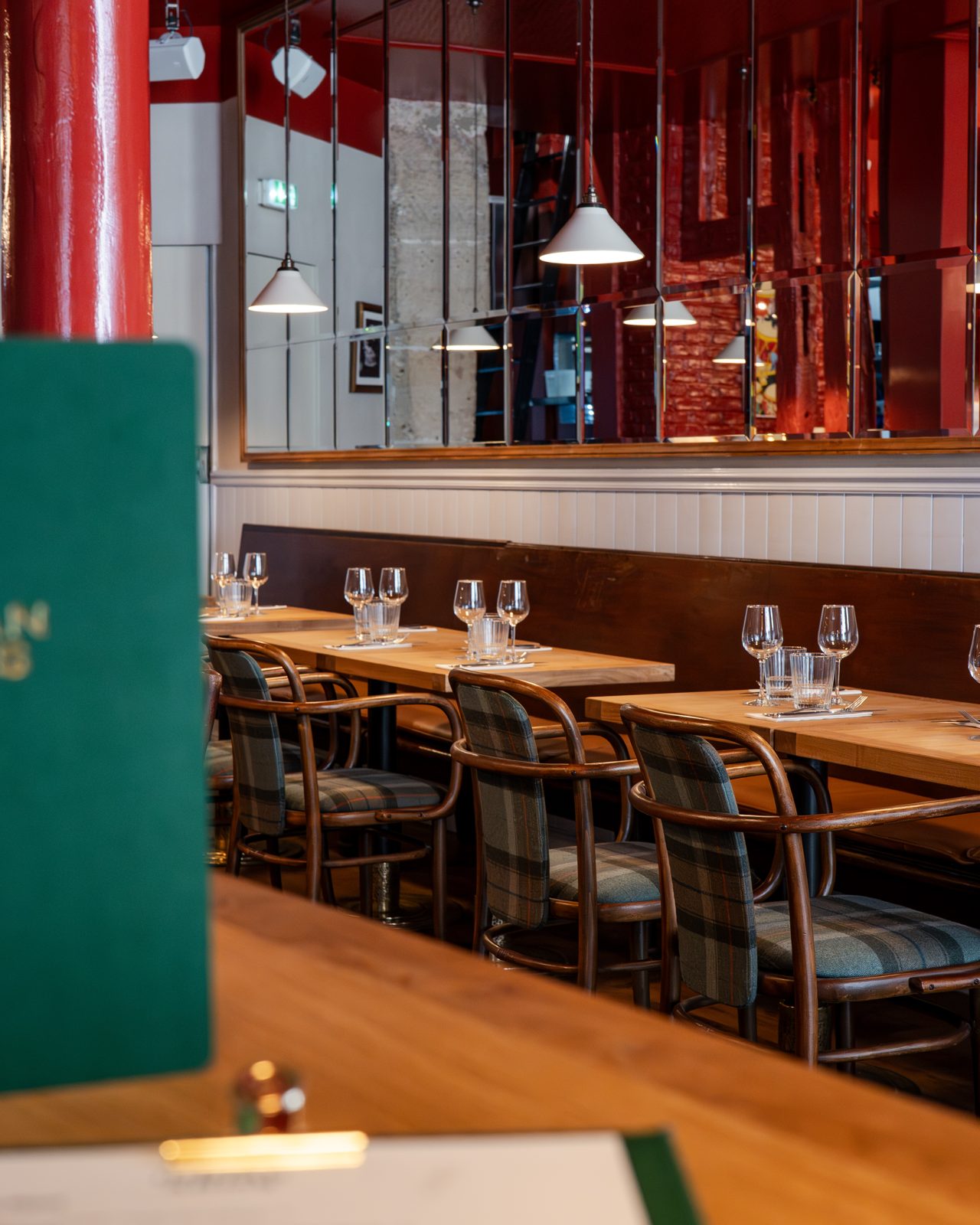 Salle du gastropub The Indian Arms avec banquettes rouges, tables en bois et suspensions