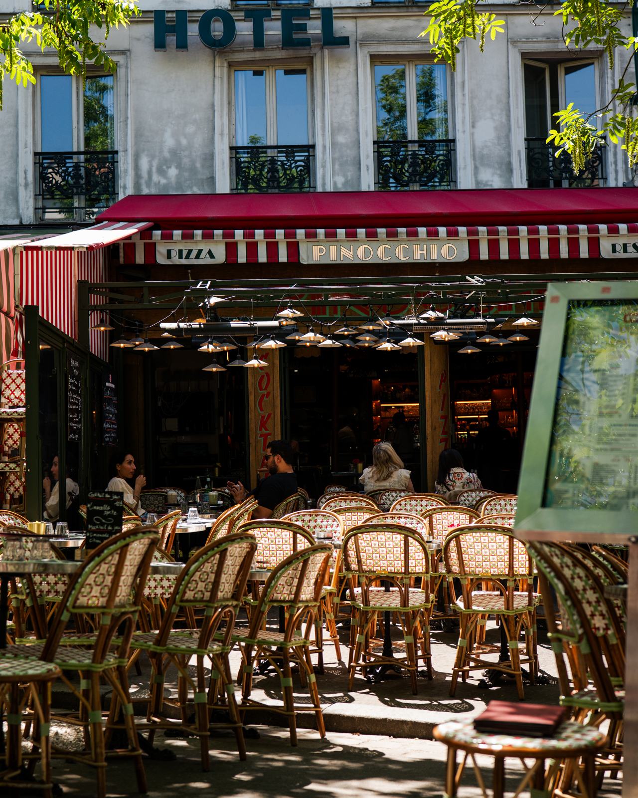 Terrasse de la brasserie Pinocchio à Montparnasse avec chaises en rotin et auvent rouge