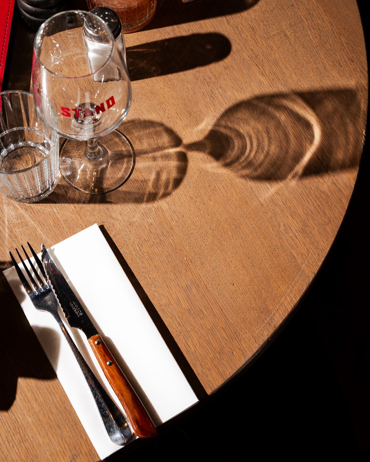 Verre et couverts posés sur une table ronde en bois baignée de lumière