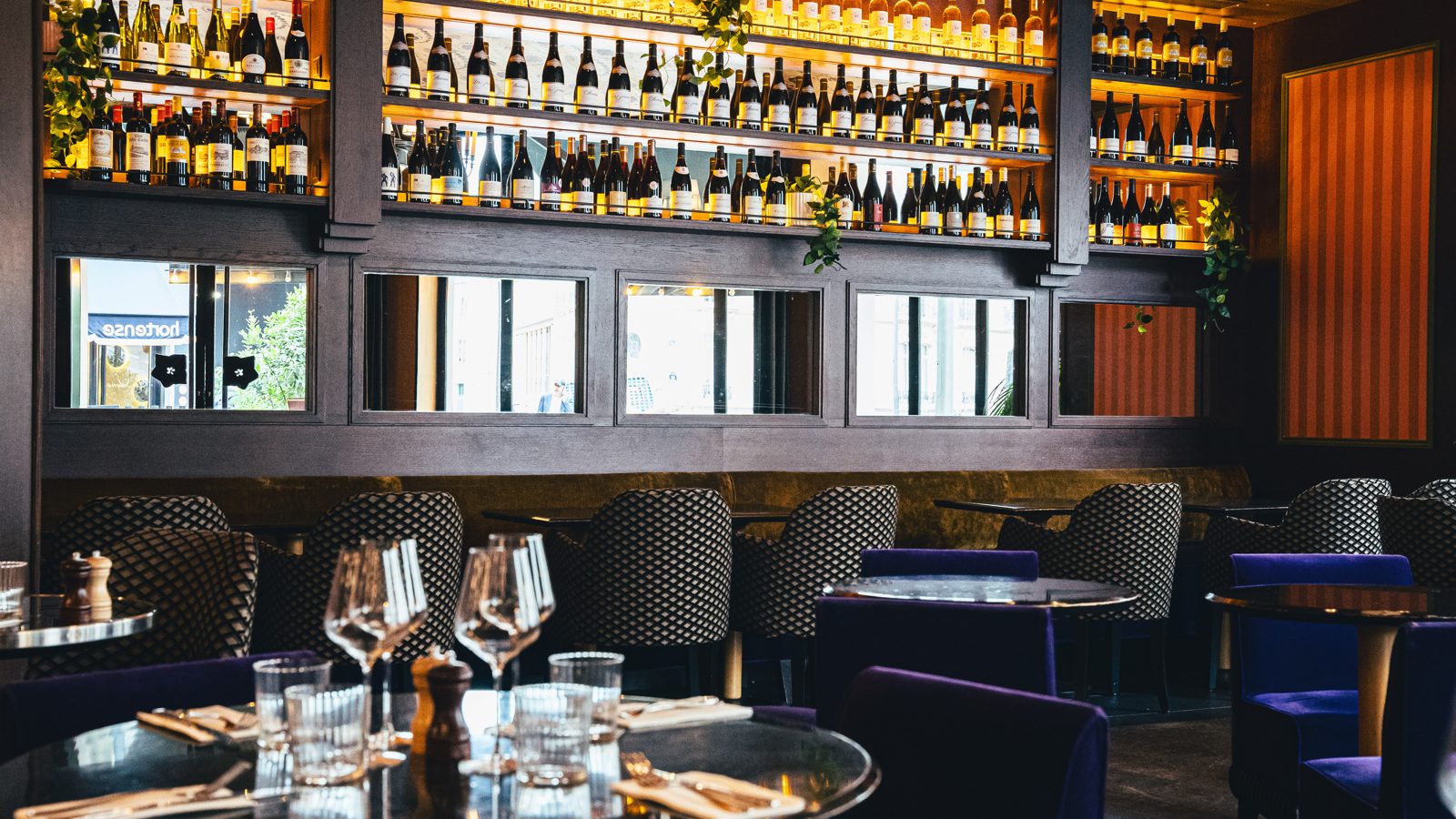 Salle de restaurant d'hôtel avec banquettes en velours, tables dressées et bibliothèque de bouteilles