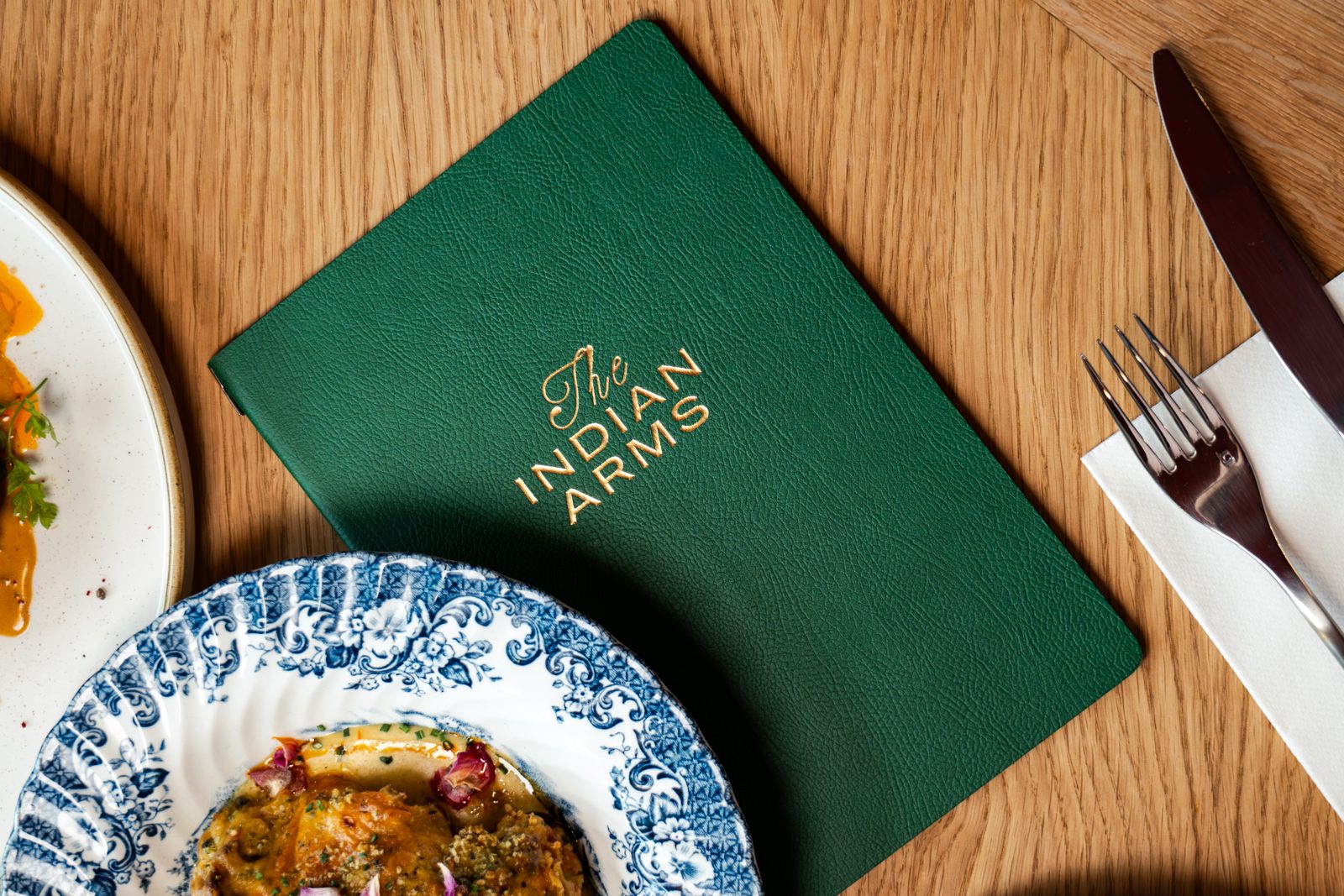 Menu vert de The Indian Arms posé sur une table à côté d'une assiette